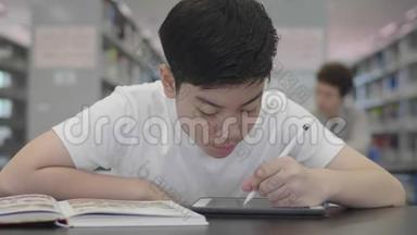 亚洲预科男孩使用<strong>平板</strong>电脑在图书馆。 两个男孩<strong>微笑</strong>着在<strong>平板</strong>电脑上画画。